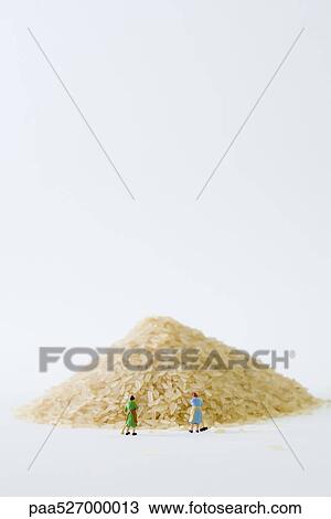 Stock Image - Miniature women sweeping large pile of rice. Fotosearch