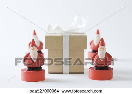 Picture - Santa Claus figurines arranged around Christmas gift. Fotosearch