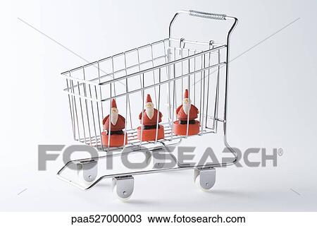 Stock Image - Shopping cart containing three Santa Claus figurines. Fotosearch