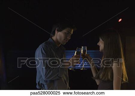 Couple clinking glasses in darkly lit room, smiling View Large Photo Image Stock Photography - Couple clinking glasses in darkly lit room, smiling. Fotosearch