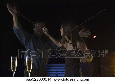 Picture - Couple dancing in nightclub, glasses of champagne in foreground. Fotosearch