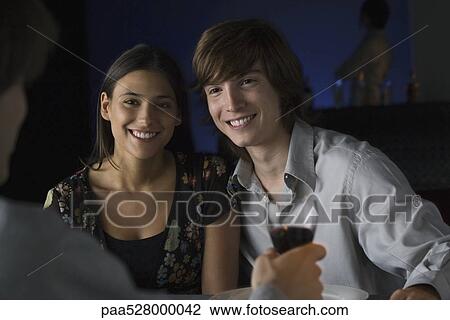 Couple sitting side by side, smiling at unrecognizable person holding glass of wine View Large Photo Image Stock Image - Couple sitting side by side, smiling at unrecognizable person holding glass of wine. Fotosearch