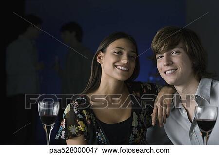 Couple smiling at camera, wine glasses in foreground, portrait View Large Photo Image Stock Photo - Couple smiling at camera, wine glasses in foreground, portrait. Fotosearch