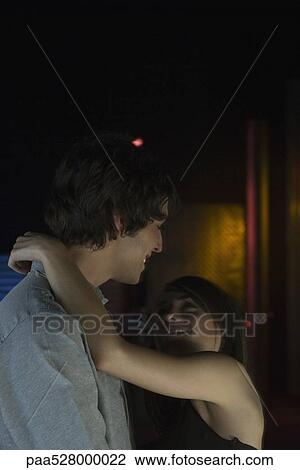 Couple standing together in darkly lit room, embracing, smiling at each other View Large Photo Image Stock Image - Couple standing together in darkly lit room, embracing, smiling at each other. Fotosearch