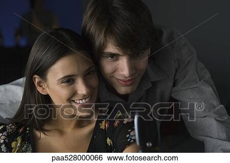 Stock Photograph - Couple together looking at cell phone, man leaning over woman's shoulder. Fotosearch