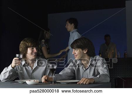 Stock Photo - Friends having wine together at nightclub, smiling at each other, couple dancing in background. Fotosearch