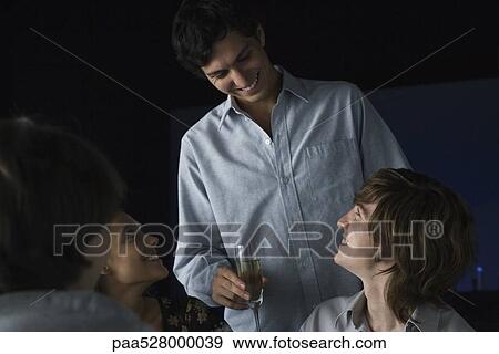 Stock Photo - Man holding glass of champagne talking to friends . Fotosearch