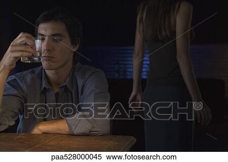 Man holding up glass of whiskey, contemplating colors, woman in background View Large Photo Image Stock Photography - Man holding up glass of whiskey, contemplating colors, woman in background. Fotosearch