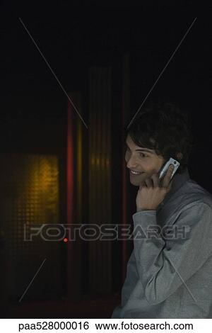 Man in darkly lit room using cell phone, listening, smiling, looking away View Large Photo Image Stock Photograph - Man in darkly lit room using cell phone, listening, smiling, looking away. Fotosearch