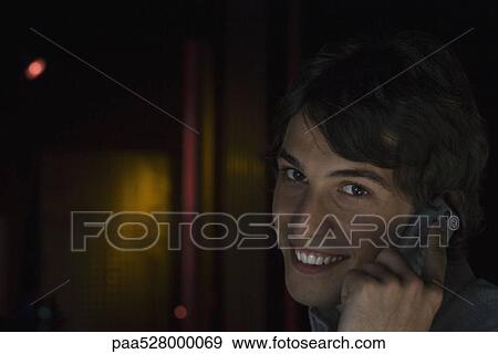 Stock Photo - Man listening to cell phone, smiling at camera, portrait. Fotosearch
