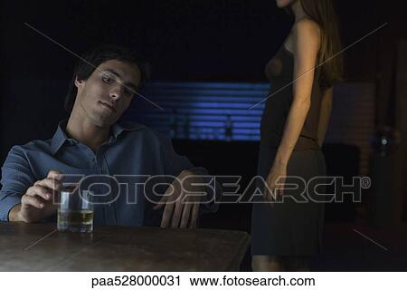Man sitting at table in bar running finger along rim of glass of whisky, woman standing nearby View Large Photo Image Stock Image - Man sitting at table in bar running finger along rim of glass of whisky, woman standing nearby. Fotosearch