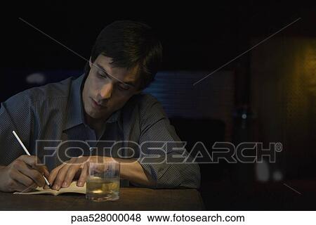 Stock Photo - Man writing in notebook, sitting in bar. Fotosearch