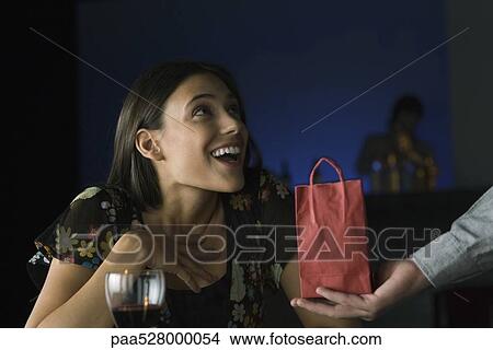 Picture - Woman being presented with gift, looking up in astonishment at giver. Fotosearch