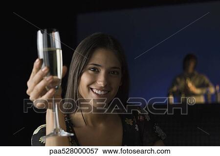 Woman holding up glass of champagne, smiling at camera, bartender in background View Large Photo Image Stock Photo - Woman holding up glass of champagne, smiling at camera, bartender in background. Fotosearch