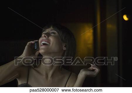 Woman talking on cell phone in darkly lit room, head back, laughing View Large Photo Image Stock Photo - Woman talking on cell phone in darkly lit room, head back, laughing. Fotosearch