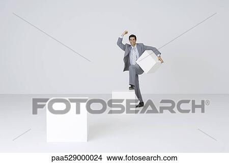 Businessman carrying block, stepping onto larger block View Large Photo Image Picture - Businessman carrying block, stepping onto larger block. Fotosearch