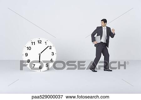 Businessman carrying document, looking over shoulder, surprised, at clock View Large Photo Image Stock Photo - Businessman carrying document, looking over shoulder, surprised, at clock. Fotosearch