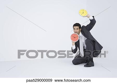 Businessman holding up two clocks View Large Photo Image Stock Photo - Businessman holding up two clocks. Fotosearch