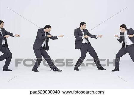 Stock Image - Businessman playing tug-of-war with clones of self, digital composite. Fotosearch