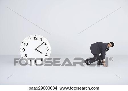 Businessman racing against time, looking over shoulder at large clock View Large Photo Image Picture - Businessman racing against time, looking over shoulder at large clock. Fotosearch