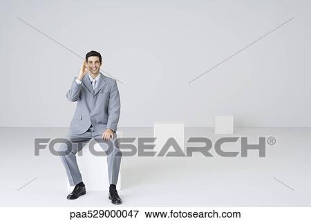 Stock Photo - Businessman sitting, making ok sign, smiling at camera. Fotosearch