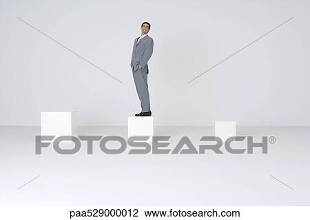 Businessman standing on block with hands in pockets, smiling at camera View Large Photo Image Stock Image - Businessman standing on block with hands in pockets, smiling at camera. Fotosearch
