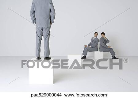 Two identical businessmen whispering over shoulders, third businessman watching View Large Photo Image Picture - Two identical businessmen whispering over shoulders, third businessman watching. Fotosearch