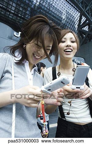 Stock Image - Female friends looking at cell phones and laughing. Fotosearch