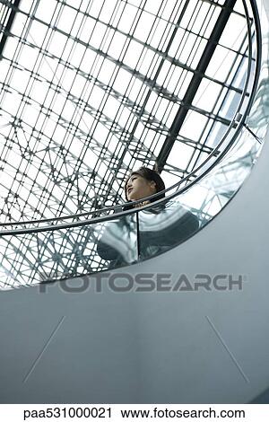 Stock Image - Female leaning against railing, looking away, low angle view. Fotosearch