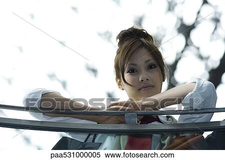 Stock Photography - Female leaning against railing, smiling at camera, low angle view. Fotosearch