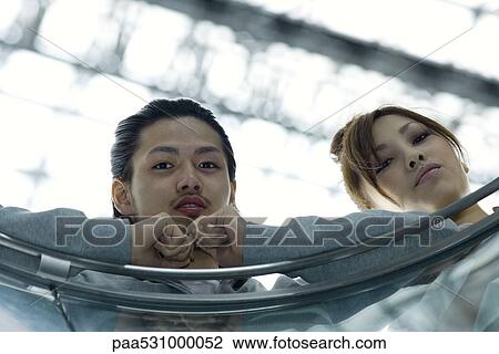Stock Image - Friends leaning against railing, looking at camera, low angle view. Fotosearch