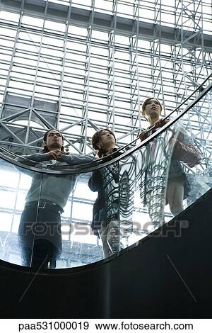 Stock Photo - Friends leaning against railing, looking up, low angle view. Fotosearch