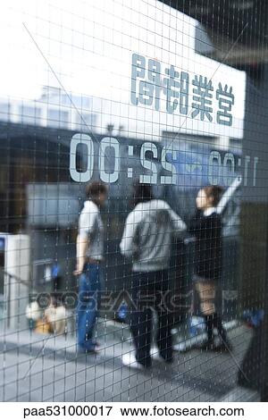 Stock Photo - Glass door printed with Japanese text and hours, people standing in background. Fotosearch