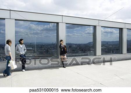 Three young friends leaning against glass wall overlooking city, Kyoto, Japan View Large Photo Image Stock Photography - Three young friends leaning against glass wall overlooking city, Kyoto, Japan. Fotosearch