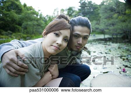 Stock Photograph - Young couple crouching beside pond, portrait. Fotosearch