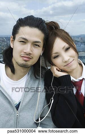 Young couple sharing earphones, smiling View Large Photo Image Picture - Young couple sharing earphones, smiling. Fotosearch