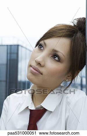 Stock Image - Young female leaning head against wall, looking up, portrait. Fotosearch