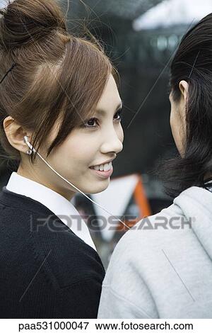 Stock Photo - Young female listening to earphones, smiling at boyfriend, cropped view. Fotosearch