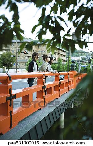 Young friends standing on bridge, looking at view View Large Photo Image Stock Photograph - Young friends standing on bridge, looking at view. Fotosearch