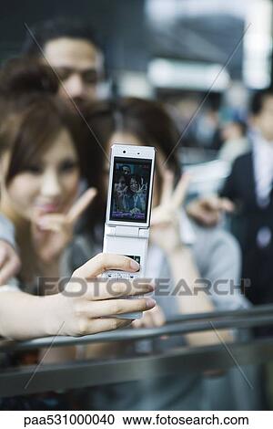 Stock Image - Young friends taking self-portrait with cell phone, focus on cell phone. Fotosearch