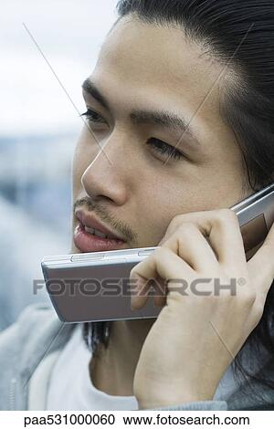 Stock Image - Young male using cell phone, looking away. Fotosearch