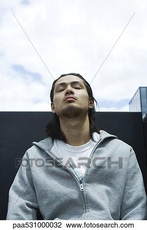 Young man sitting outdoors with head back, eyes closed View Large Photo Image Stock Image - Young man sitting outdoors with head back, eyes closed. Fotosearch