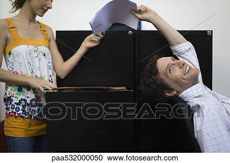 Stock Image - Man leaning back in chair, handing document to woman. Fotosearch