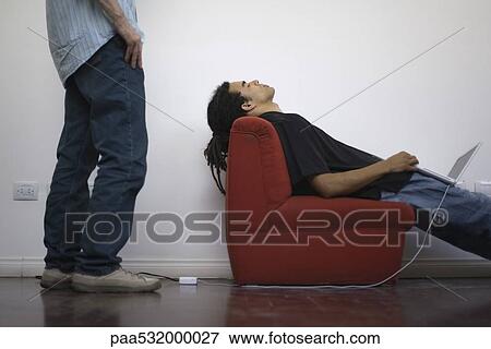 Man napping in chair with laptop balanced on lap, colleague standing behind watching View Large Photo Image Stock Photo - Man napping in chair with laptop balanced on lap, colleague standing behind watching . Fotosearch