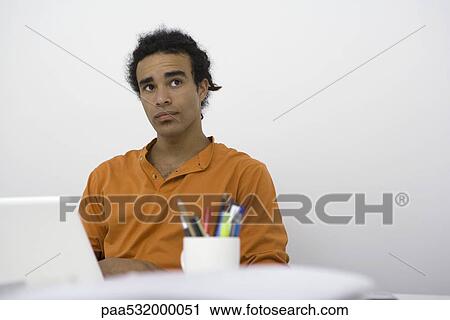 Stock Image - Man sitting at desk, looking up in thought. Fotosearch
