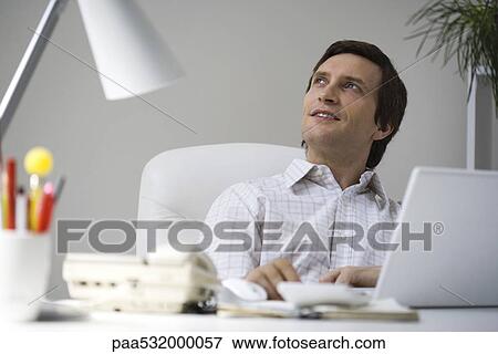 Man sitting at desk, looking up View Large Photo Image Stock Photo - Man sitting at desk, looking up. Fotosearch