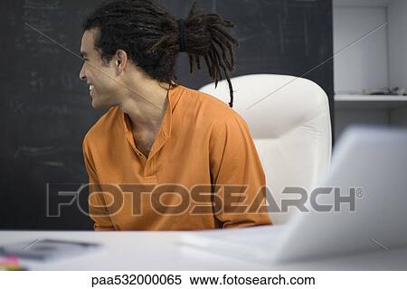 Man sitting at desk, smiling over shoulder View Large Photo Image Stock Photography - Man sitting at desk, smiling over shoulder. Fotosearch