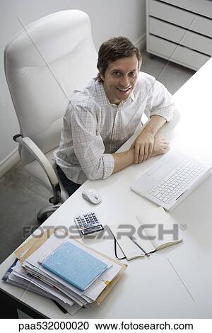 Man sitting at desk, smiling up at camera View Large Photo Image Stock Image - Man sitting at desk, smiling up at camera. Fotosearch