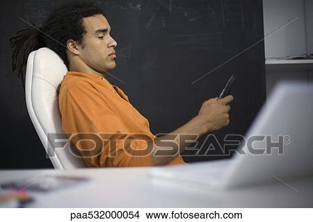 Man sitting in chair, looking down at cell phone View Large Photo Image Picture - Man sitting in chair, looking down at cell phone. Fotosearch