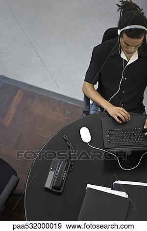 Stock Photo - Man working at laptop, listening to headphones, overhead view. Fotosearch
